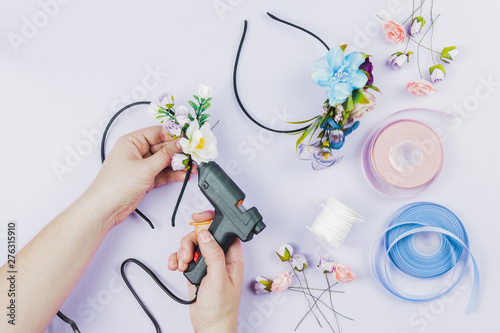 Close-up of woman's hand sticking the flowers on hairband with electric hot glue gun on white backdrop photo