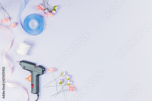 Electric hot glue gun; thread spool; ribbon and artificial roses isolated on white backdrop