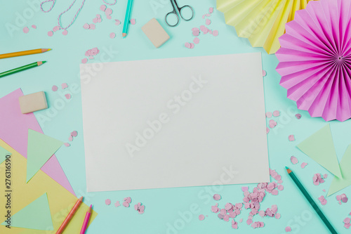 White blank paper with confetti; colored pencils; scissor and eraser on turquoise backdrop