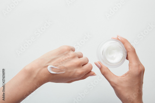 cropped view of woman applying cream on skin and holding jar isolated on white