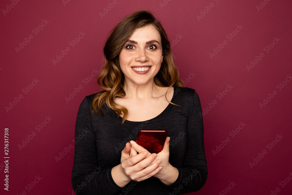 Female exited person holding red mobile standing indoor on the pink background