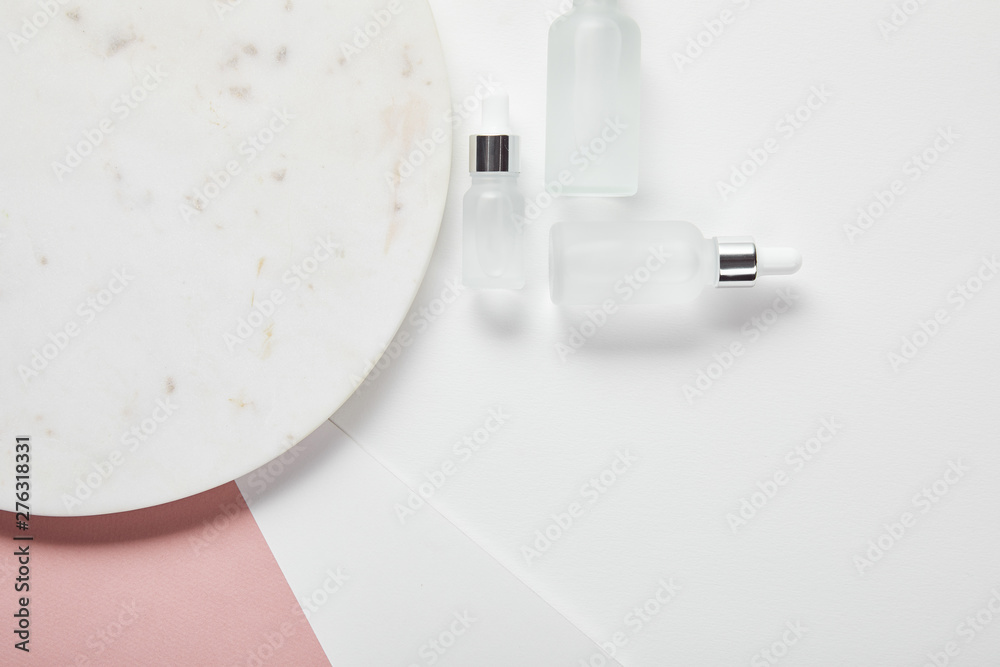 Fototapeta premium top view of cosmetic glass bottles near plate on white pink surface
