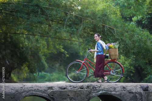 Beautiful woman with red bike And flower basket On a bridge over a stream in the forest