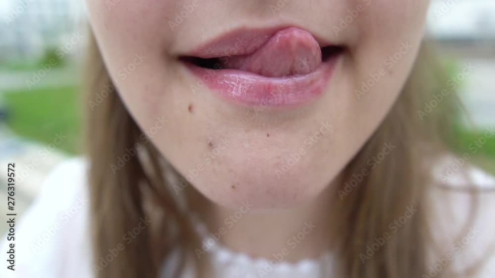 Macro close up on woman with seductive facial expression sticking out his tongue licking his lips. Portrait of flirty young woman looking at camera.