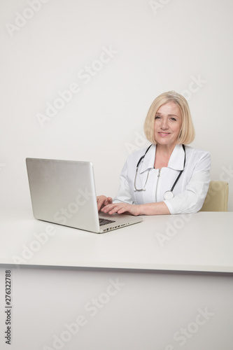 Woman doctor in a white medical clothes sitting in cabinet and working on a laptop