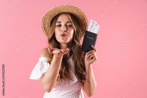 Pleased young pretty woman posing isolated over pink wall background holding passport with tickets blowing kisses.