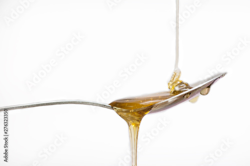 Honey dripping from a silver spoon on isolated white background