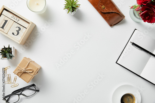 top view of blocks with numbers and letters, notepad, pen, case, glasses, plants and candle on white surface