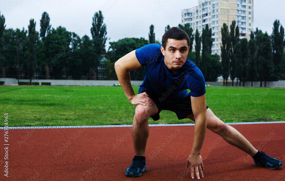 Obraz premium Young man stretching and preparing on the stadium in blue shirt