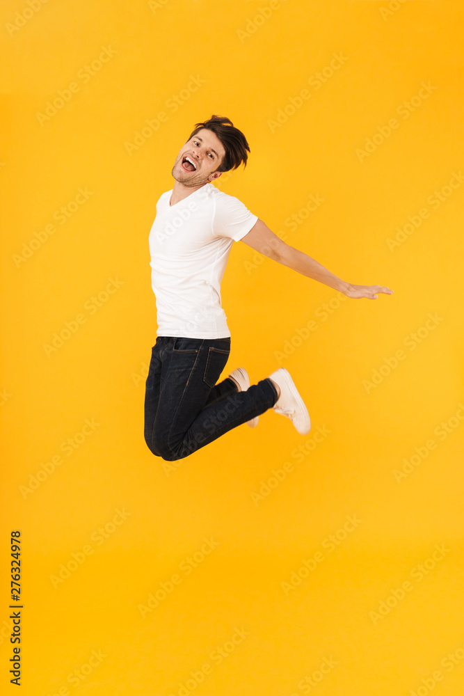Full length photo of cheerful man in basic t-shirt rejoicing and jumping with spreading arms aside Full length photo of cheerful man in basic t-shirt rejoicing and jumping with spreading arms aside