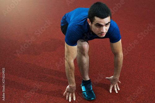 Young sportsman low starting to run on a red trackin blue shirt photo