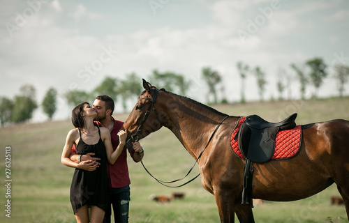 Young couple is hugging and kissing next to a horse.