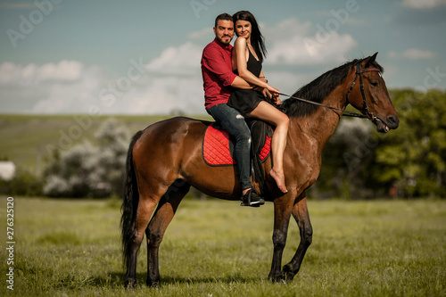 Young couple is riding a brown horse.