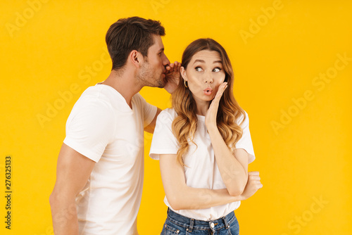 Portrait of masculine man whispering secret or interesting gossip to pretty woman in her ear