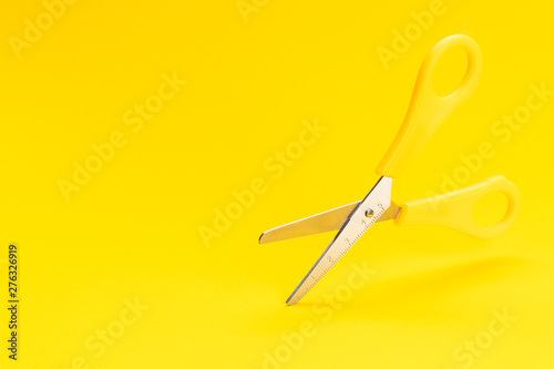 photo of levitating scissors over vivid yellow background with copy space. Conceptual image of yellow plastic open scissors floating in air over yellow background.