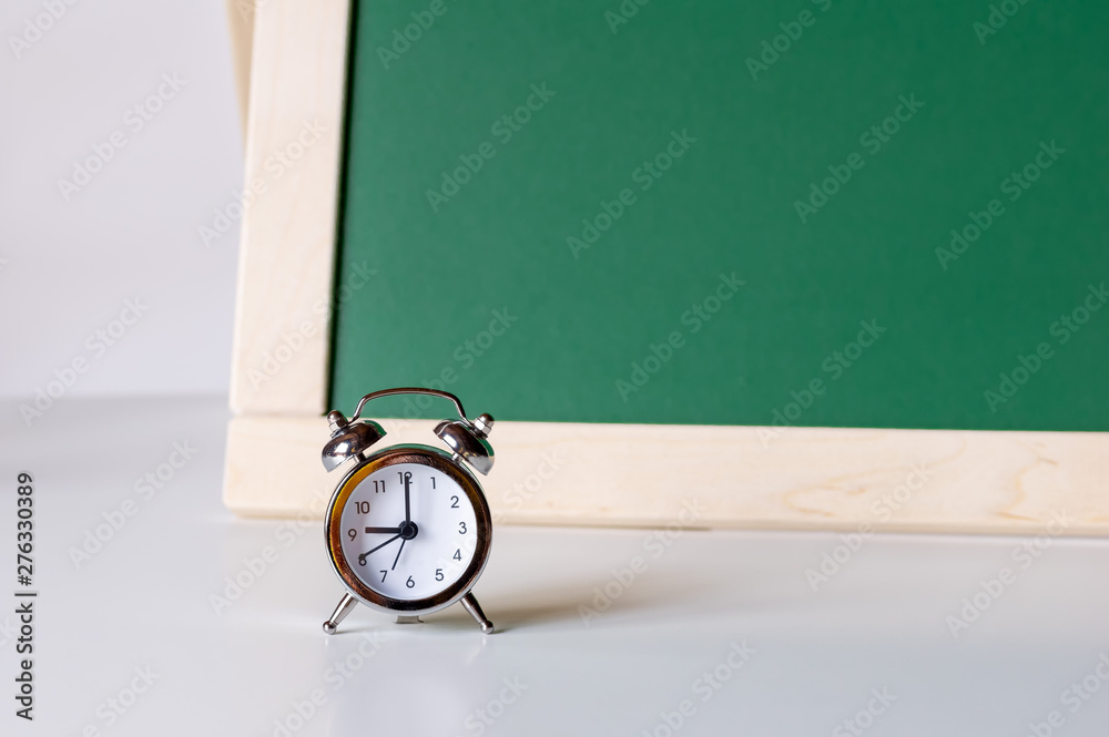 Back to school. Alarm clock on the background of the school board. School background with space for your text.