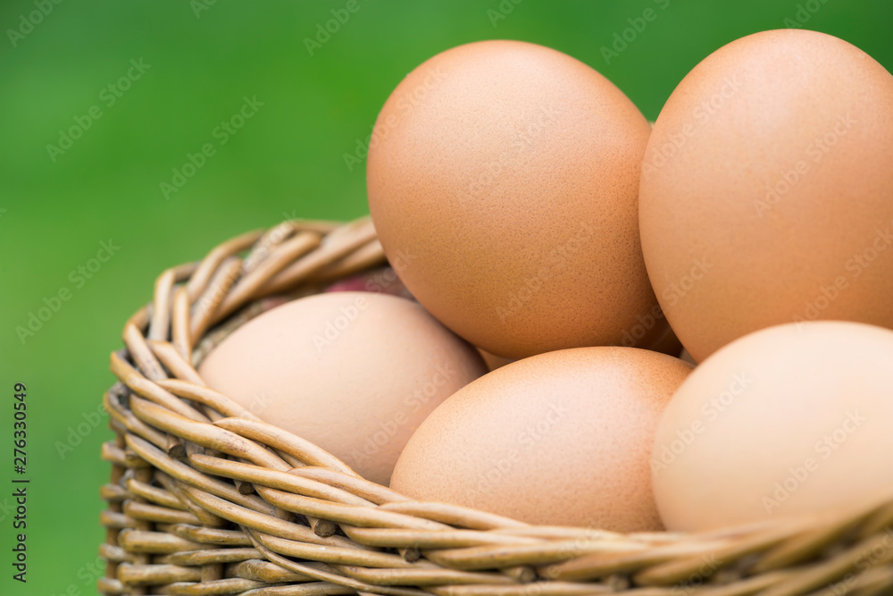 Close-up of fresh eggs in a basket on green background - obrazy, fototapety, plakaty 