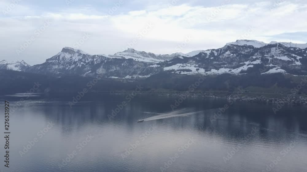 Aerial drone shot of a barge sailing across a lake surrounded by snow covered mountains and trees Aerial drone shot of a barge sailing across a lake surrounded by snow covered mountains and trees