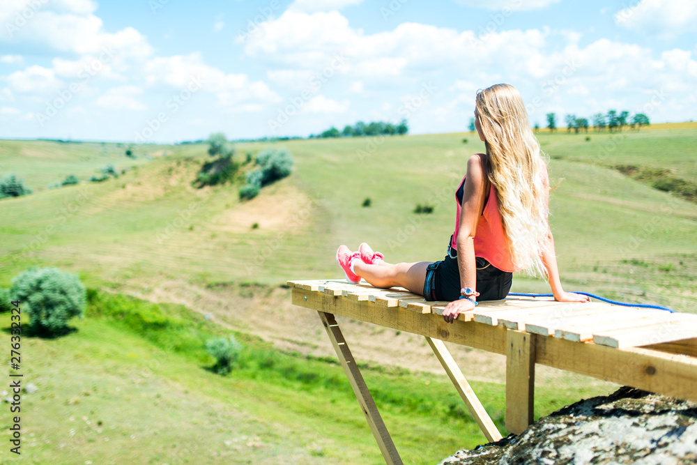 Woman sitting on a wooden ledge on a high mountain and view of the mountain landscape. A young tourist woman enjoys the scenery in the mountains.