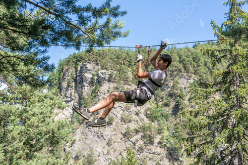 Teenager zip-lining on high ropes course, adventure, park, climbing trees in a forest in summer