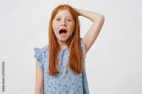 Schilderij op canvas Portrait of screaming petite freckles red-haired girl, wears in blue dress, looks angry, stands over pink background