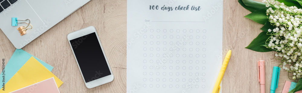 panoramic view of stationery, 100 days check list, flowers and smartphone on wooden table panoramic view of stationery, 100 days check list, flowers and smartphone on wooden table