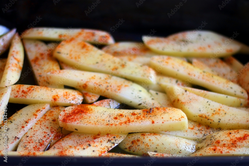 Pan with cut potatoes, dressed with olive oil, basil and smoked paprika. Selective focus.