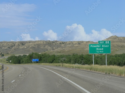 Medium close up of a scenic winding road with directional signs to Powder River Road and rest area.