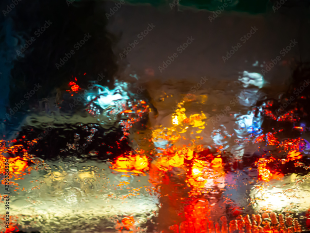 Blurred rain drops on car window with road light bokeh on rainy season abstract background