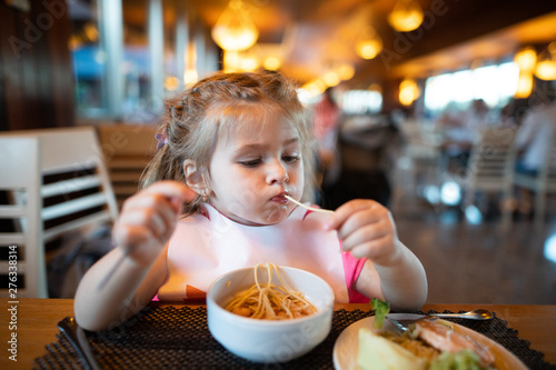 Litle girl is eating pasta in the restaurant.