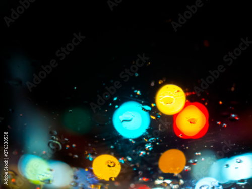 Fototapeta Naklejka Na Ścianę i Meble -  Blurred rain drops texture on car window with colorful bokeh abstract background on the road.