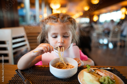 Litle girl is eating pasta in the restaurant.