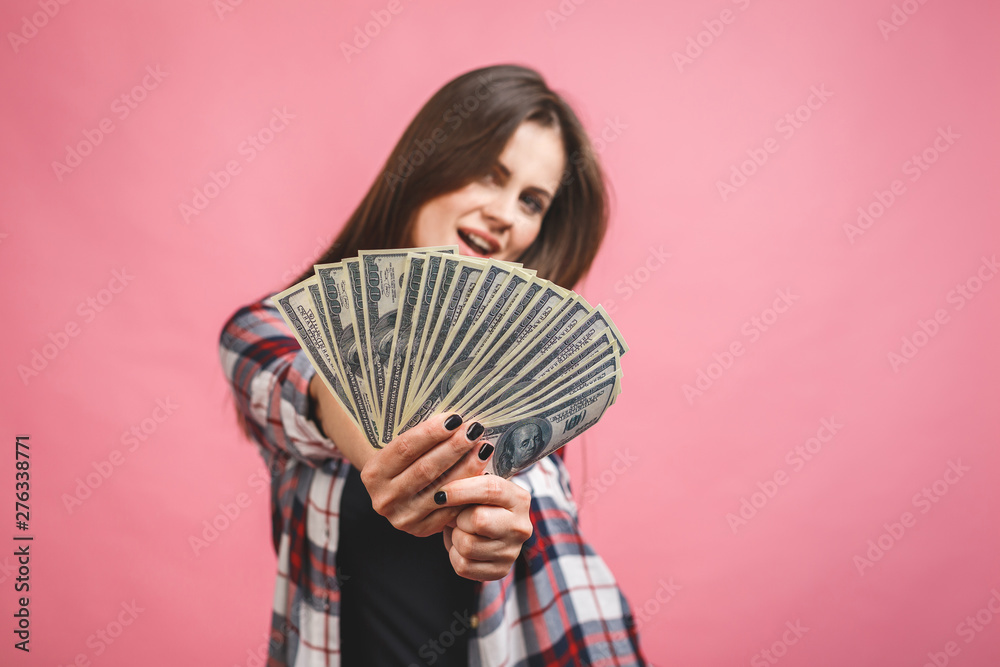 Portrait of a cheerful young woman holding money banknotes and celebrating isolated over pink background. Portrait of a cheerful young woman holding money banknotes and celebrating isolated over pink background.