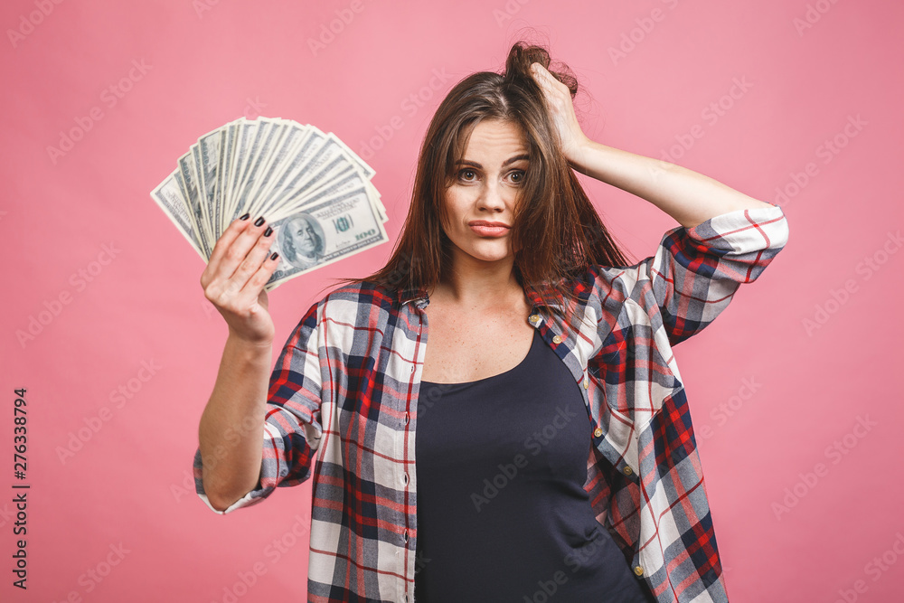 Portrait of a cheerful young woman holding money banknotes and celebrating isolated over pink background. Portrait of a cheerful young woman holding money banknotes and celebrating isolated over pink background.