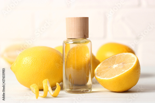 Bottle of essential oil of lemon and lemons on a light background