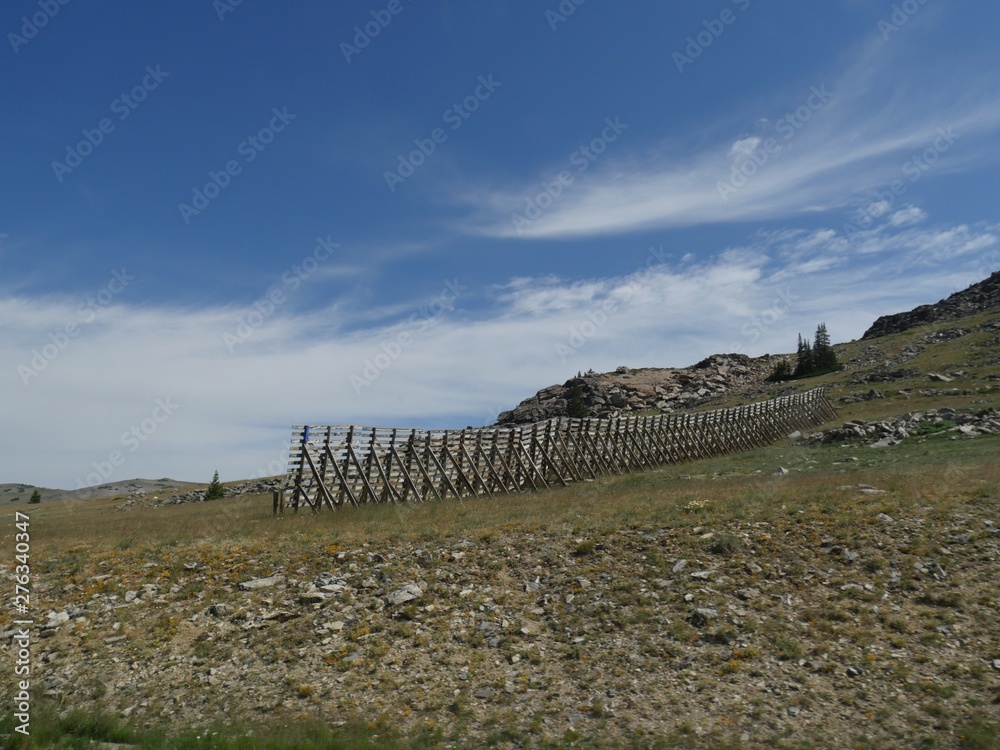 Hillside view with a high wooden fence on a beautiful day in Wyoming.