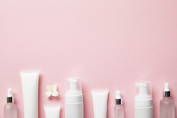 top view of cosmetic glass bottles, cream tubes with cream, cosmetic dispensers and jasmine flower on pink