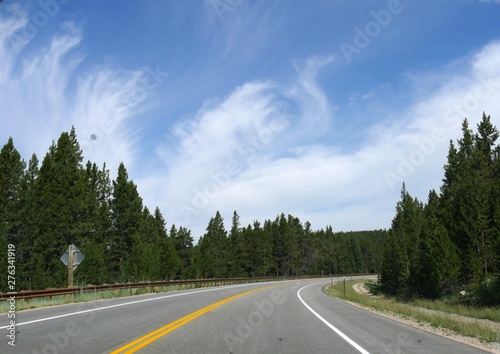 Curbing road with lush forests and beautiful cloud formations in the skies at Bighorn County in Wyoming.