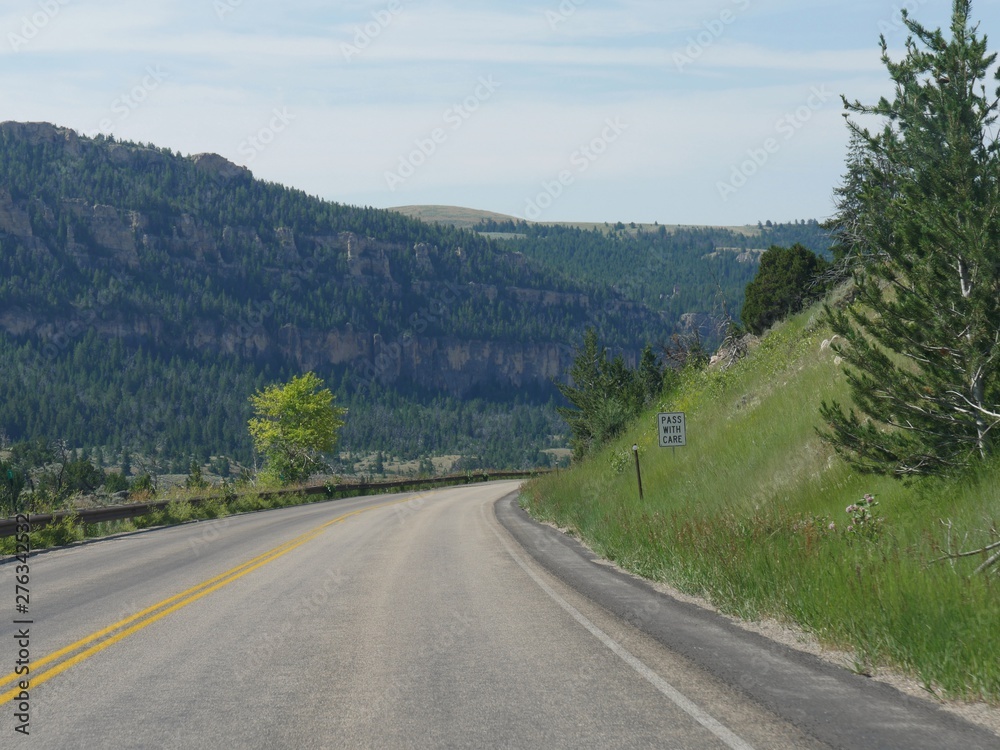 Sharp twists and turns in the road along deep ravines and high cliffs with a road side sign warning drivers to pass with care at Bighorn Mountains in Wyoming.