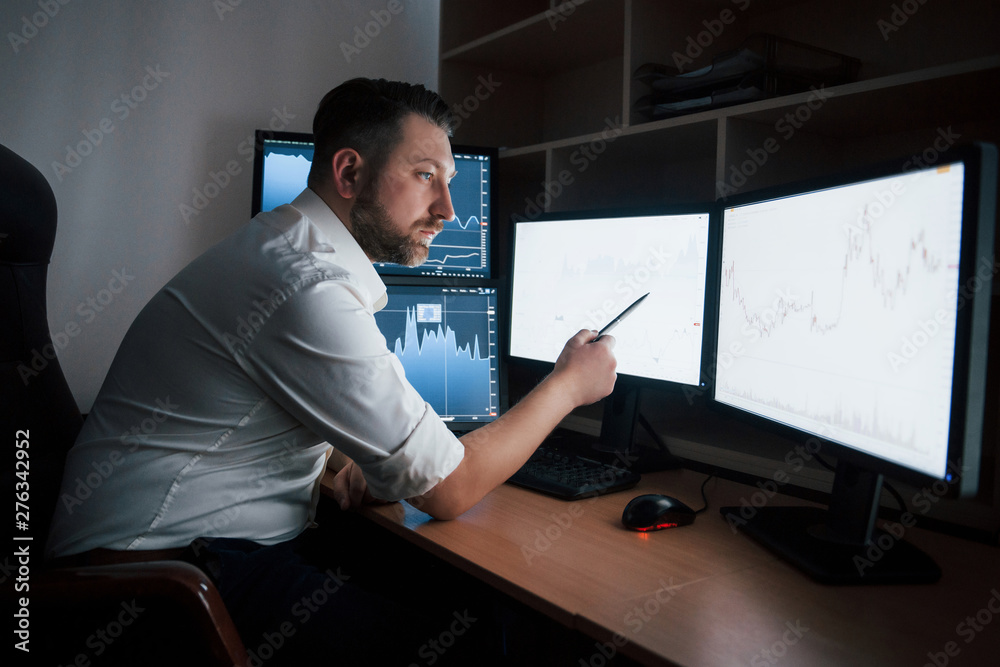 So many monitors. Bearded man in white shirt works in the office with multiple computer screens in index charts So many monitors. Bearded man in white shirt works in the office with multiple computer screens in index charts