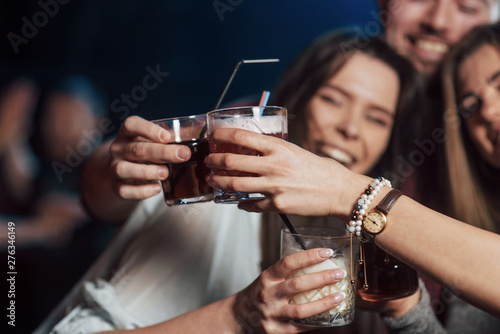 Traditional knocking glasses process. Group of young friends smiling and making a toast in the nightclub