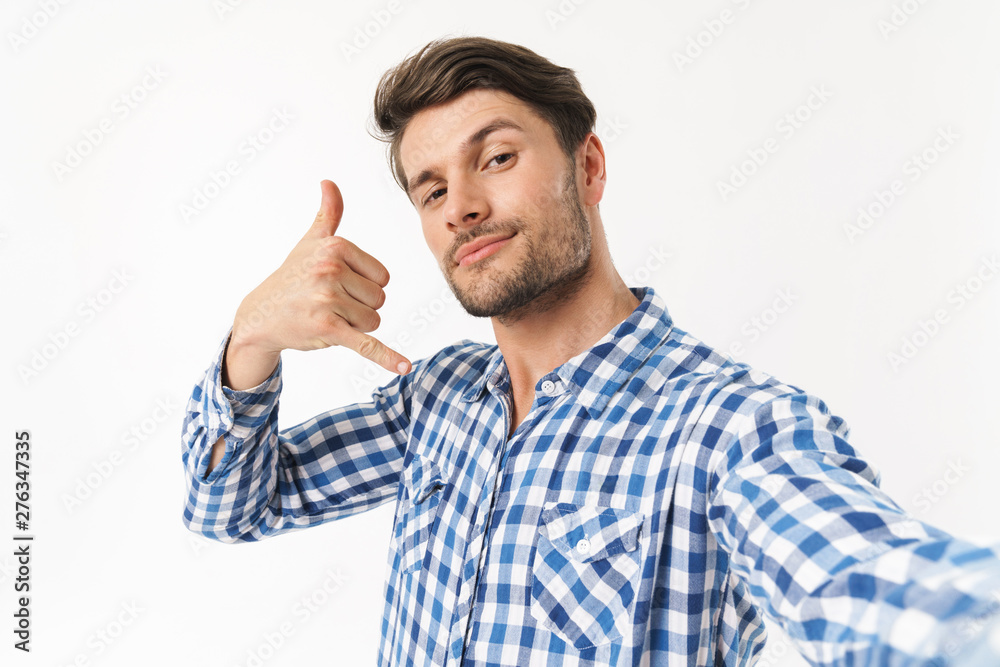 Handsome young unshaved man dressed in casual shirt posing isolated over white wall background take a selfie by camera gesturing with hand. Handsome young unshaved man dressed in casual shirt posing isolated over white wall background take a selfie by camera gesturing with hand.