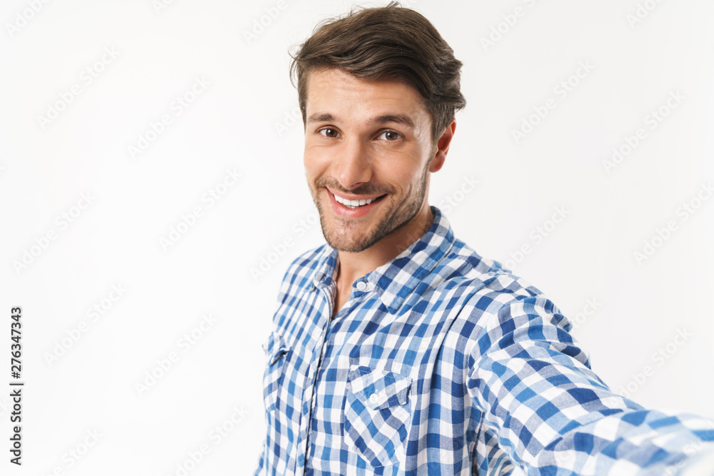 Optimistic happy young unshaved man dressed in casual shirt posing isolated over white wall background take a selfie by camera. Optimistic happy young unshaved man dressed in casual shirt posing isolated over white wall background take a selfie by camera.