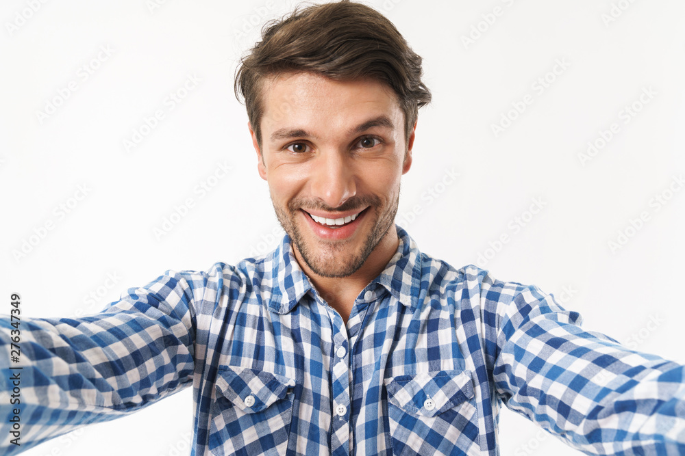 Happy young unshaved man dressed in casual shirt posing isolated over white wall background take a selfie by camera. Happy young unshaved man dressed in casual shirt posing isolated over white wall background take a selfie by camera.