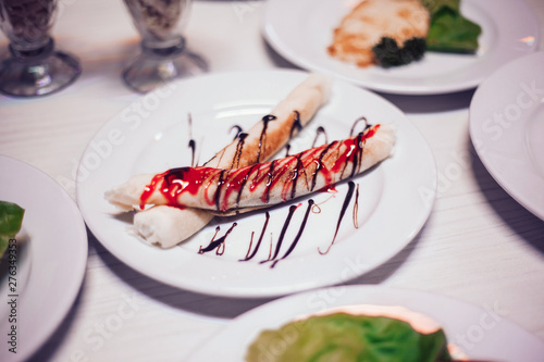 thin blinchiki with sweet sauce, hamburger and other dishes on the table in the cafe