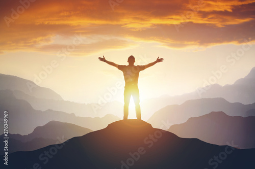 Man standing on edge of mountain feeling victorious with arms up in the air. photo