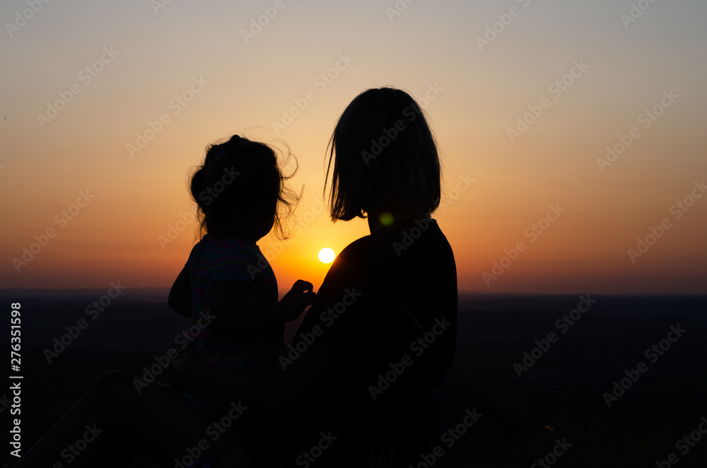 Mother and daughter who sit and look at the sunset .