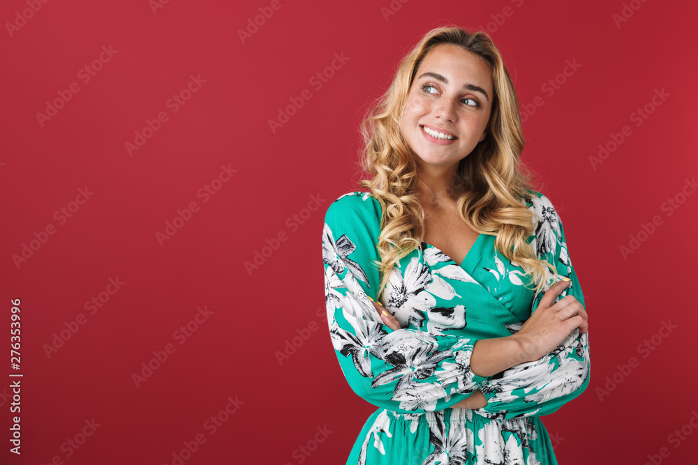 Cheerful happy cute young blonde girl in bright blue dress posing isolated over red wall background looking aside. Cheerful happy cute young blonde girl in bright blue dress posing isolated over red wall background looking aside.