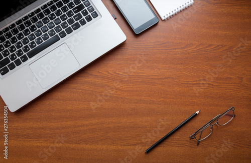 Wood office desk table with laptop, glasses, notebook, pen, smartphone. Top view, copy space