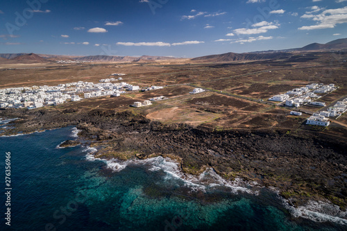 Drone view of a spanish island, volcano beach, blue sky, clouds , white houses on the coast, pastel tons, Lanzarote. 